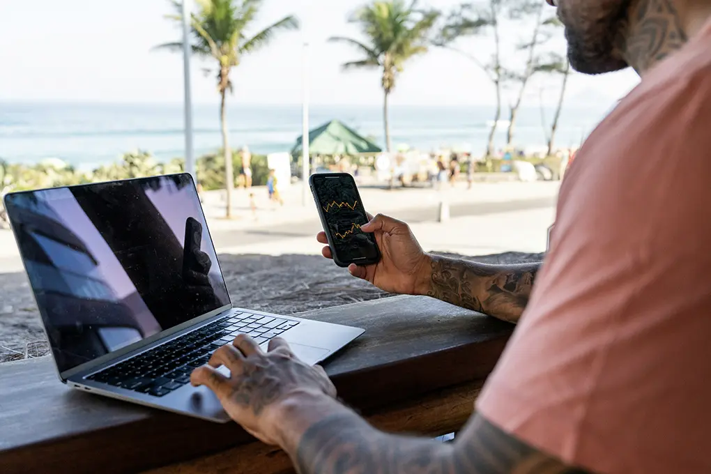Man at the beach on his laptop and a phone