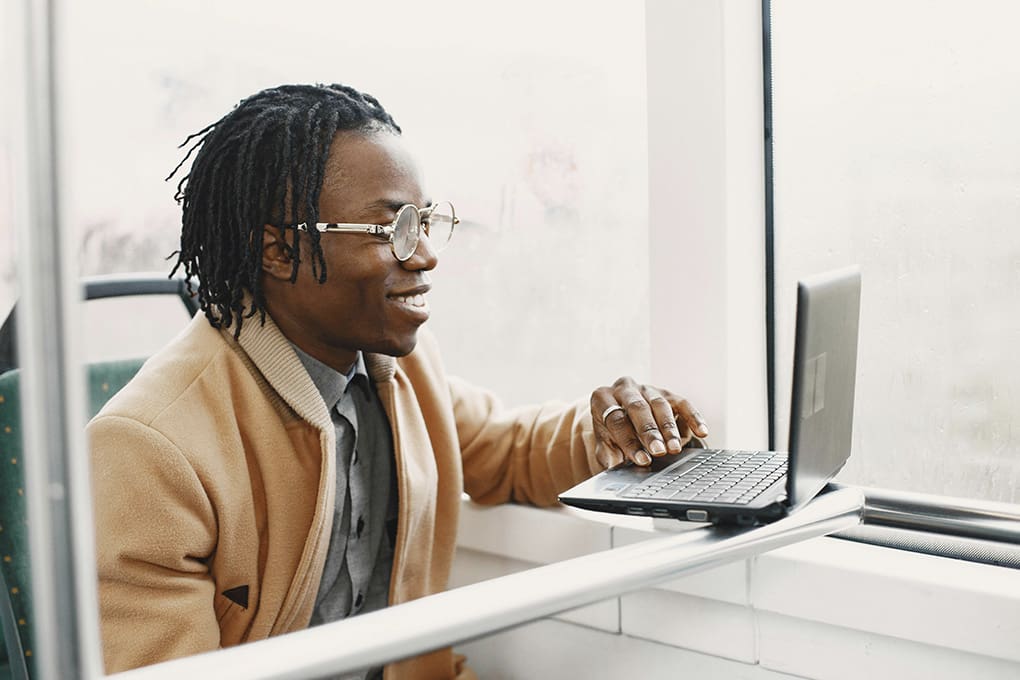 A man is working on a laptop and smiling, as if he is attending a video conference