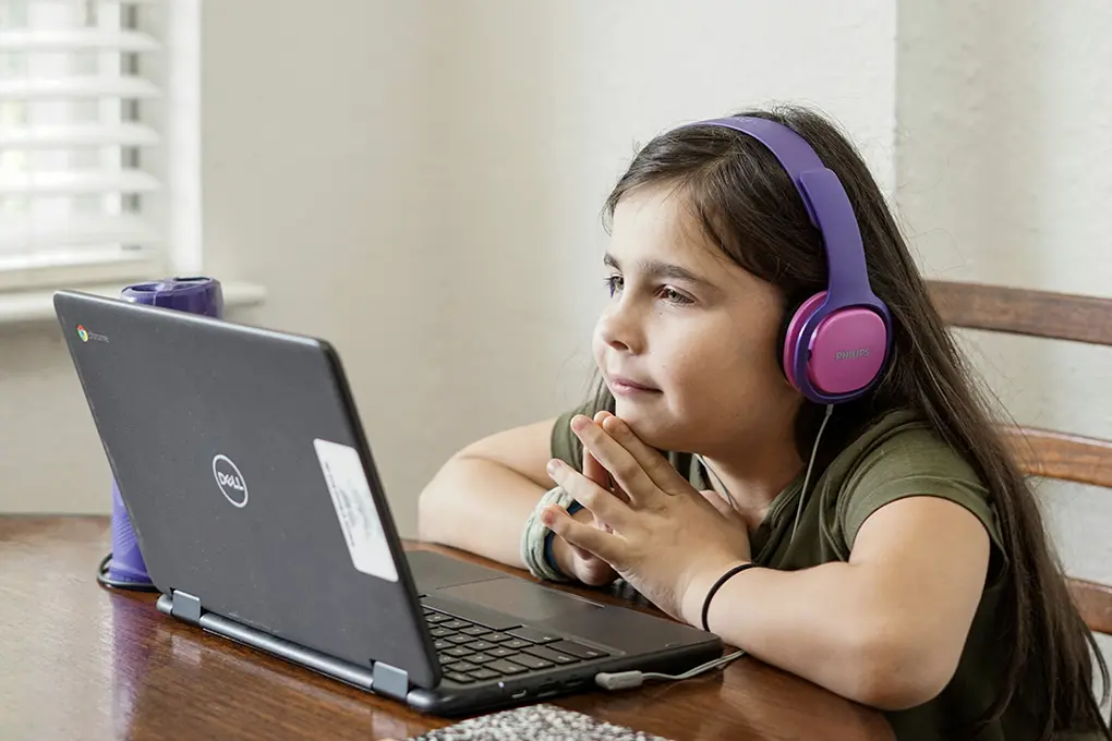 Young girl wearing purple headphones, intently watching a laptop screen at a table