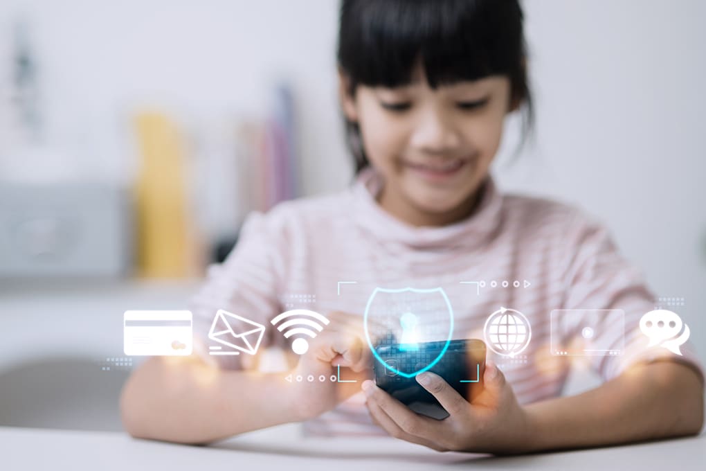A smiling child using a smartphone with digital security icons overlaid, including a shield, credit card, email, wifi, globe, and chat bubbles.
